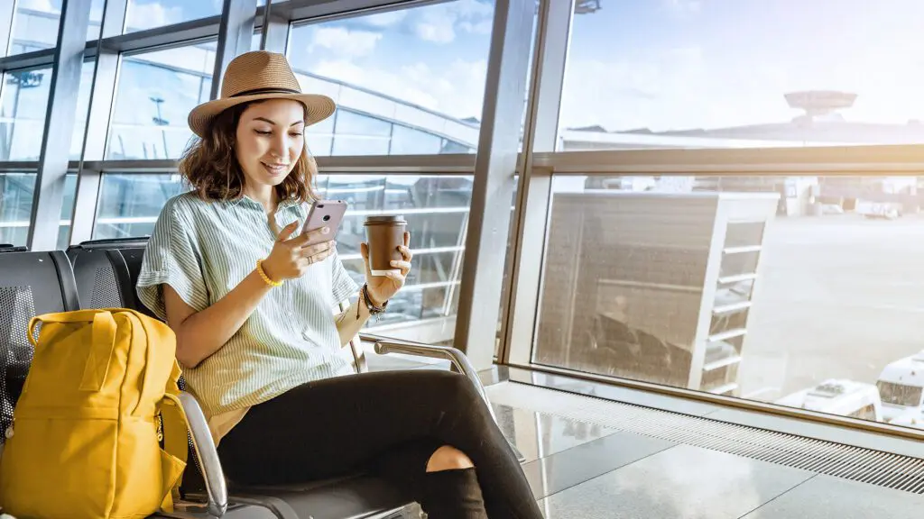 Digital ID in air travel: Smiling young woman in airport lounge looks at her phone