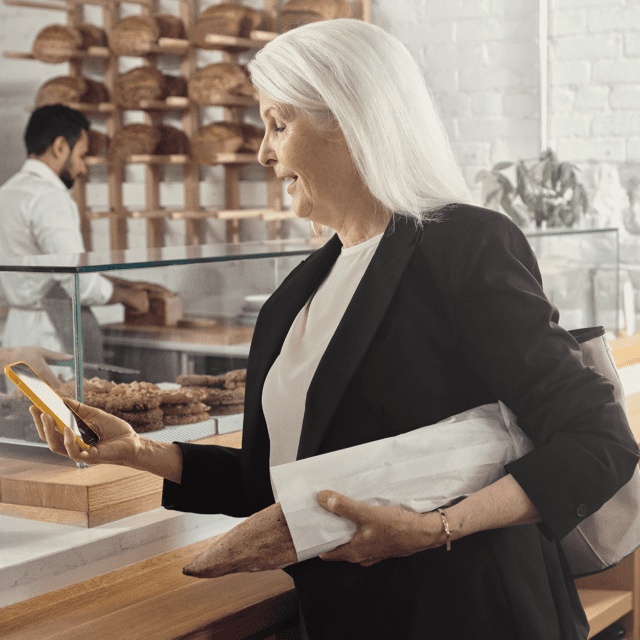 A woman in a business suit looks at her mobile phone in a café, smiling thanks to faster payments.
