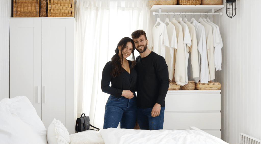 Standing centred in a white, elegantly decorated bedroom, the Hornyaks hug, facing the camera.