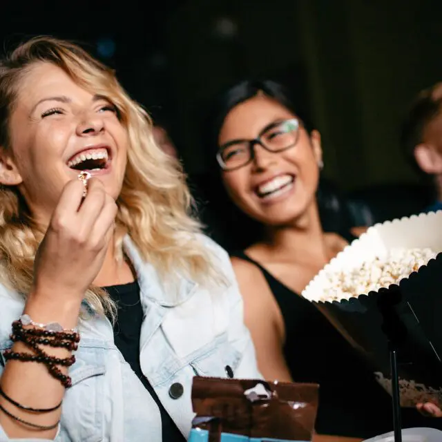 Friends enjoying popcorn and watching a movie at a cinema.