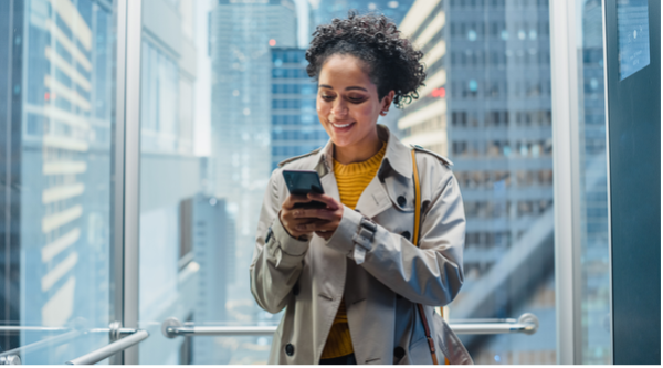A woman riding in a glass elevator smiles at her smart phone.