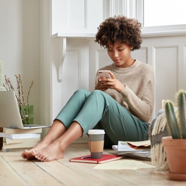 A seated young woman looks at her smartphone, updating her data security.