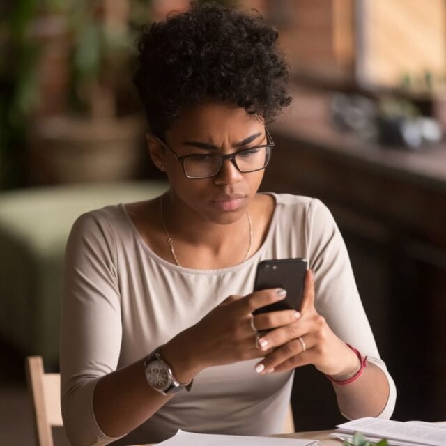 A woman looks intently at a smartphone screen. Avoid e-transfer scams by spotting email fraud.