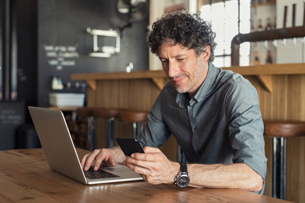 Person making a mobile payment or Interac e-Transfer from his smartphone while doing business on a laptop