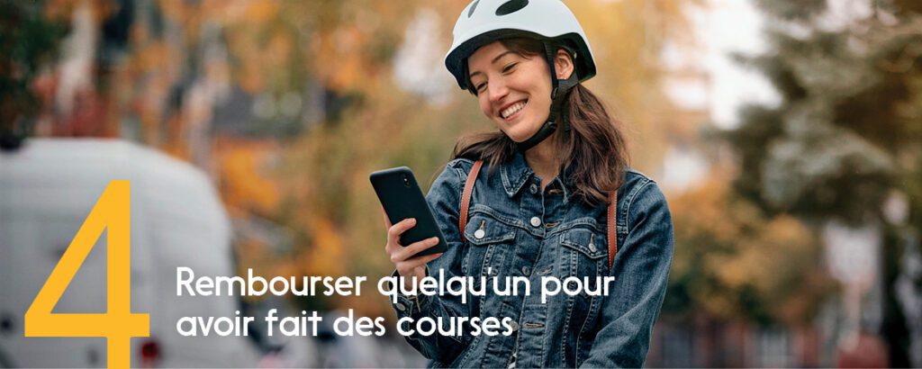 Une femme portant un casque de vélo blanc sourit quand elle reçoit un paiement sur son téléphone. 