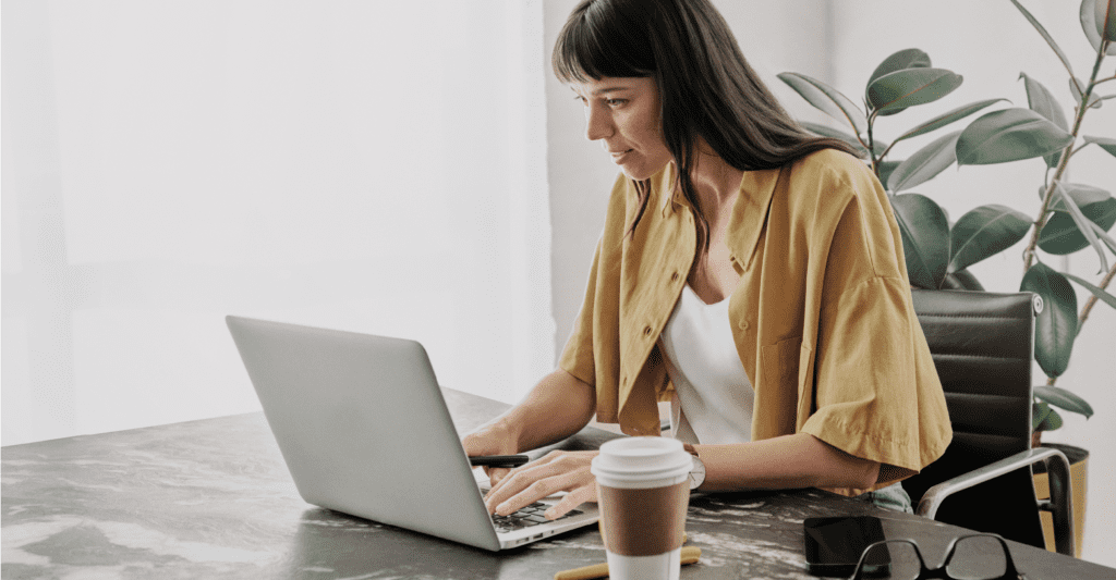 A woman seated at a desk uses a laptop.