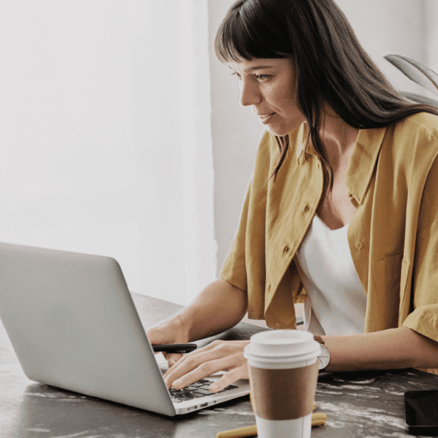 A woman seated at a desk uses a laptop.