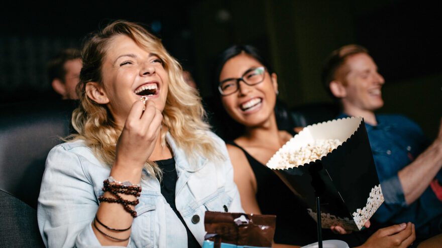 Friends enjoying popcorn and watching a movie at a cinema.