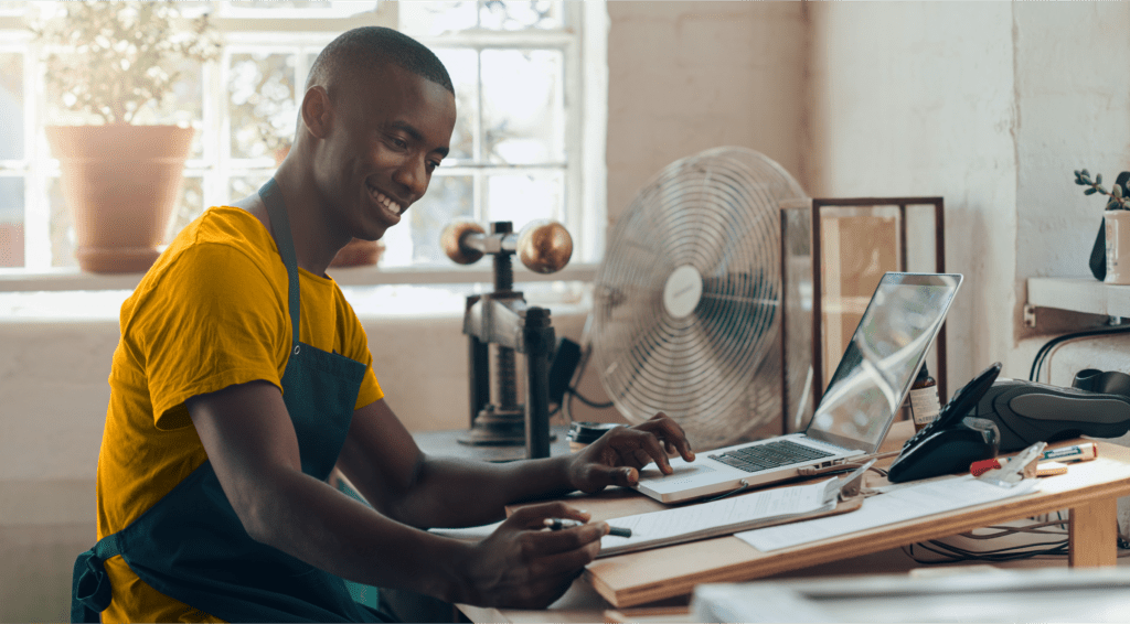 A small business owner smiling while he works on his computer and with a clipboard