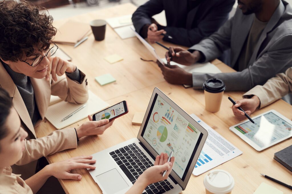 A group of people in work attire sit at a table working with digital devices.