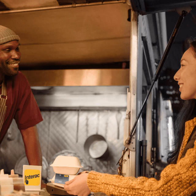 Woman in yellow sweater making INTERAC Debit transaction at a small business