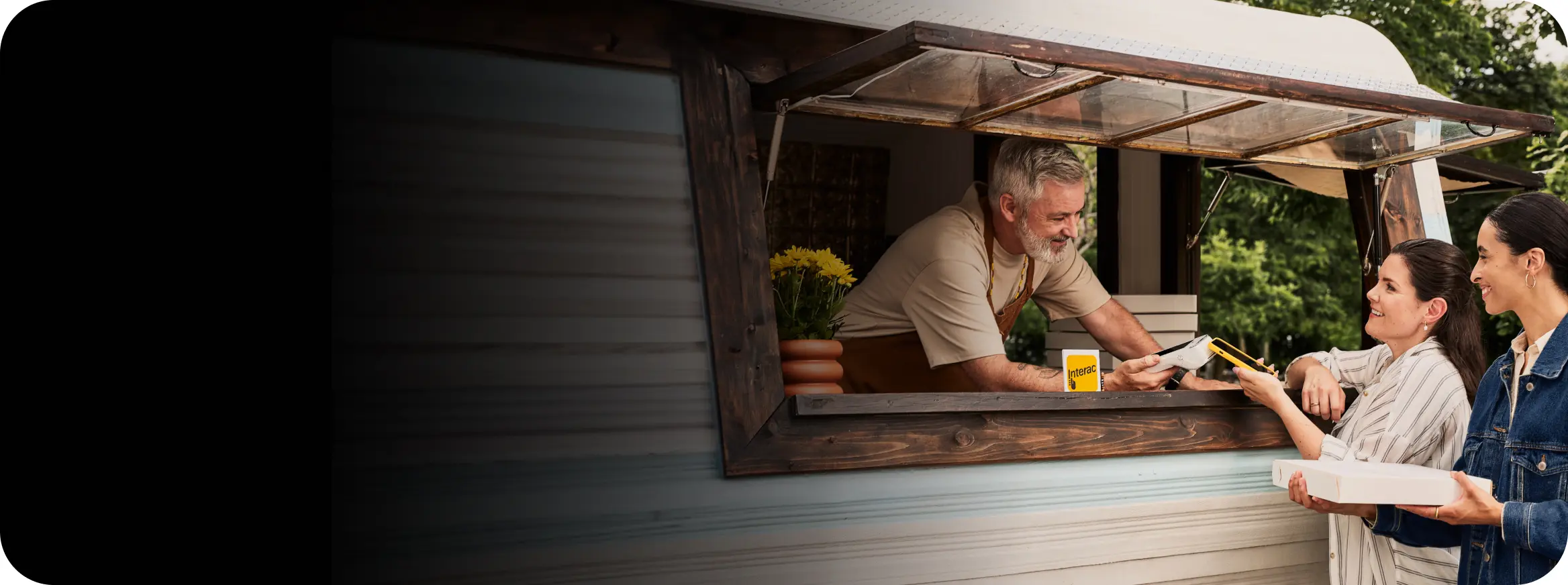 A man working inside a food-vending stall leans forward to offer payment terminal.
